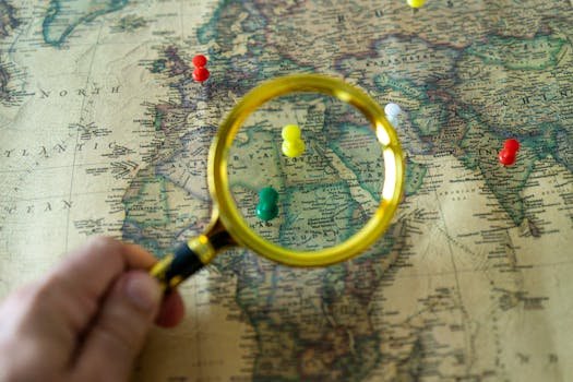 Close-up of a hand holding a magnifying glass over a world map with colorful pins indicating travel destinations.